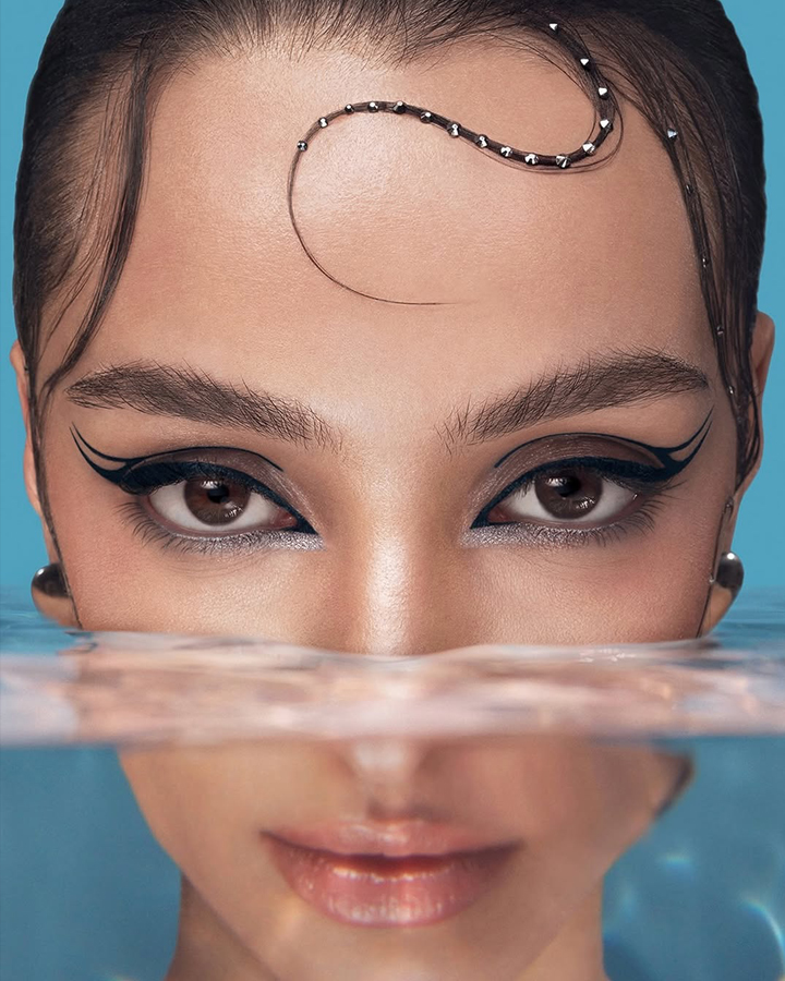 Close up of a model with graphic liner making eye contact with the camera emerging from wate